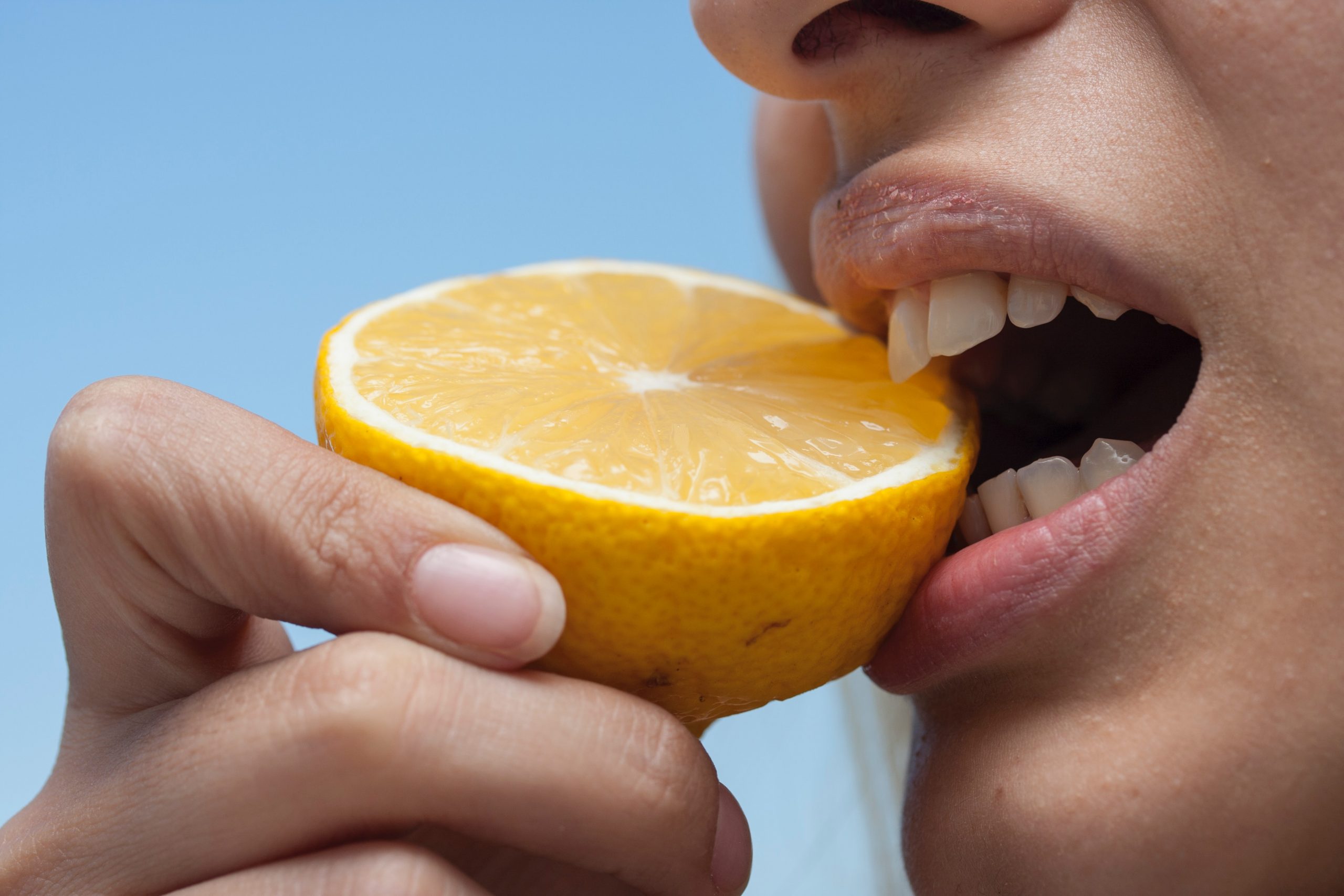 Biting half of lemon with exposed teeth.
